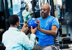 Man in blue shirt sits on bosu ball with physical therapist after Georgia Workers Compensation Accident